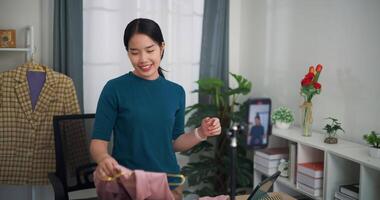 Footage dolly shot, Young asian woman business owner stand selling clothes while live streaming on mobile phone show new collection fashion clothes to customer ,Online Shopping video