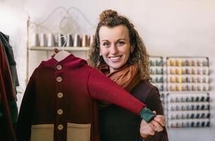 A smiling woman with curly hair holds a red jacket in a quaint boutique photo