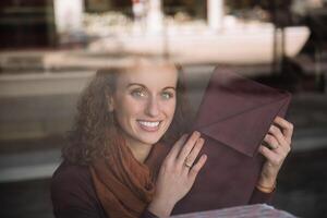 Radiant woman with curly hair, seen through a shop window, smiling as she holds up a piece of fabric, showcasing a joyful shopping moment photo