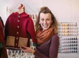 Woman with curly hair showcasing a fashionable red and tan jacket, standing in a boutique decorated with threads and sewing accessories photo