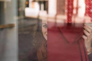 alegre mujer con Rizado pelo echar un vistazo mediante un vaso ventana en un animado urbano ambiente foto