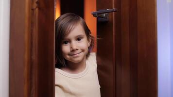 un pequeño niña abre el puerta a el habitación y mira fuera desde detrás el puerta video