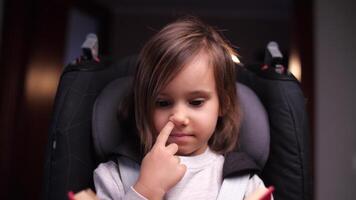 pequeño niña escoge su nariz, el niña se sienta en un niño coche asiento video