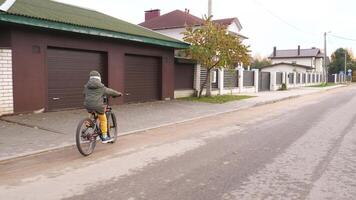 Junge Fahrten ein Fahrrad im ein klein Stadt, Dorf auf das Straße im Herbst im kalt Wetter video