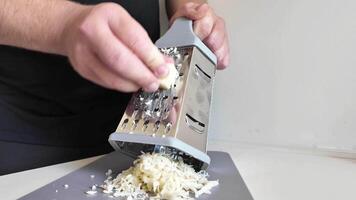 Person grating cheese with a metal grater onto a cutting board, a kitchen activity related to cooking and meal preparation concepts video