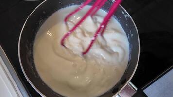 menging pannenkoek beslag in een pan met een roze vliegenmepper Aan een kookplaat, concept voor huis Koken en pannenkoek dinsdag tradities video