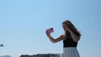 Griekenland corfu eiland jong meisje toepassingen een telefoon en duurt een foto tegen de backdrop van een vliegend vlak tegen de lucht video