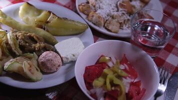 Salad with tomatoes bun with cheese Grilled zucchini, grilled peppers In a restaurant in Macedonia, food is served on a red square tablecloth. video