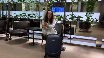 tourisme concept. une magnifique fille en jouant avec une mobile téléphone dans un aéroport. fille, valise, Téléphone, aéroport video