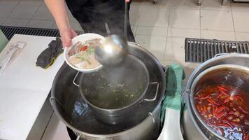 Pour broth over pho soup. The broth is light brown and there are thin slices of beef, white onions, and green onions floating on top. There are also white chopsticks video