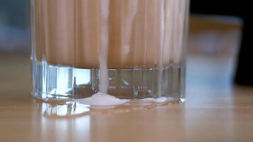Glas von ein vereist Kaffee mit Sahne Milch. kalt brauen Kaffee trinken mit Eis. früh Morgen Sonne Licht. Frappé mit Zucker Sirup Kaffee mit Milch köstlich trinken hoch Schaum rühren mit ein Stroh im ein Restaurant video