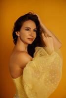 Profile portrait of a beautiful middle-aged woman in a yellow dress, her hair pulled up against a yellow background photo