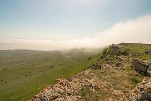 A foggy mountain top with a clear blue sky in the background. The sky is filled with clouds, giving the scene a serene and peaceful atmosphere. photo