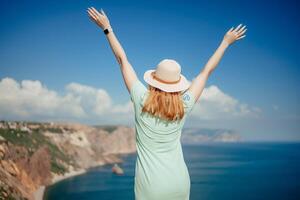 Woman tourist sky sea. Happy traveler woman in hat enjoys vacation raised her hands up photo