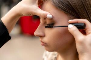 maquillaje artista pinturas pestañas a un mujer en un belleza salón. foto