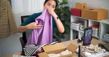 antal fot dolly skott, ung asiatisk kvinna företag ägare försäljning kläder leva strömning på mobil telefon visa ny samling mode kläder till kund ,uppkopplad handla video