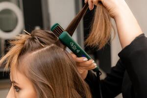 el peluquero prepara un mujer, hace un peinado con chinos utilizando un curling hierro. largo ligero marrón natural cabello. yo cuidado concepto. foto