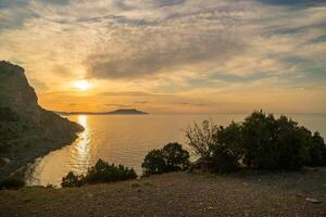 A beautiful sunset over the ocean with a rocky shoreline. The sky is filled with clouds, creating a moody atmosphere. photo