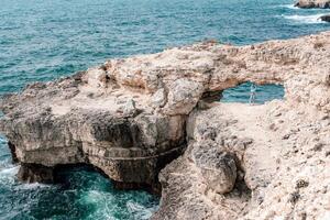 un mujer soportes en frente de un grande rock formación con su brazos extendido. concepto de libertad y aventura, como el mujer es abrazando el natural belleza de el rocoso paisaje. foto