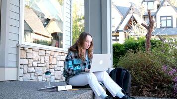 el niña terminado su estudios sentado en el porche cierra el ordenador portátil se inclina en eso mira a el lado toma agua descanso relajación después haciendo deberes bebida agua desde un botella Canadá Vancouver surrey video