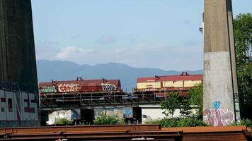 pattullo ponte al di sopra di fraser fiume treno passaggio sotto ponte. avvicinamento tiro a partire dal tecnologico luogo sparpagliato ferro travi per il costruzione di nuovo ponte contro il fondale di montagne e cielo video