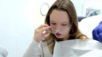 Fertig das Verfahren im das Dental Büro nehmen aus schützend Brille böse Auge und Lätzchen jung Mädchen Frau im Weiß Kleider Sitzung im Dental Stuhl Arzt im Blau Handschuhe hilft schön Menschen echt Leben video