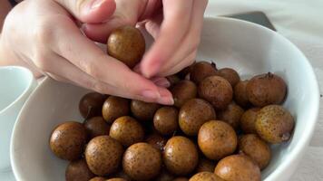 Person peeling longan fruit. sweet. tropical delicacy in Southeast Asia. by hand over a white. ceramic plate. 4k footage 2160p video