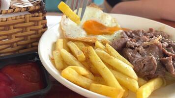 patatas con carne Cerdo y frito huevo desayuno comiendo con un tenedor de cerca disparo video