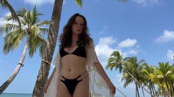 kvinna dans, löpning, hår och pareo fladdrande kvinna på tropisk havsstrand mellan palmer elegant kvinna njuter sommar resa i bikini bär solglasögon. Söt eleganta lady bär Sol hatt. video