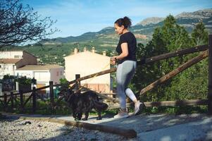 Young woman taking her dog for a walk while jogging on the morning in mountains nature on a warm sunny day photo