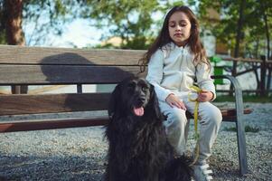 adorable pequeño niña sentado en un ciudad banco, tomando su árbol genealógico cocker spaniel perro para un caminar o el naturaleza. jugando mascotas. gente, infancia y perro como mejor compañero foto