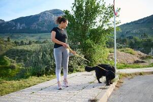 Full length portrait happy woman in taking her dog for a walk on leash in the nature. Multi ethnic enjoying walk with her pedigree purebred black cocker spaniel dog in the mountains nature outdoors photo