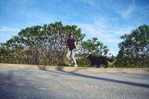 Full length authentic portrait of a cheerful woman running with her pet on leash, as perfect way to walk a dog and to exercise outdoors. Playing pets concept photo