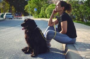 lado retrato de un pensativo joven adulto mujer sentado en el parapeto, soñando mirando dentro el distancia mientras tomando su mascota para un caminar en el naturaleza. personas y animales concepto foto