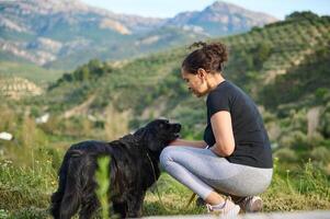 Affectionate young woman talking with her companion dog, embracing her pedigree black cocker spaniel pet while walking him in the mountains nature outdoors. Playing pets and people concept photo