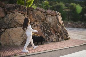 Full length portrait of a cute little child girl in sportswear, taking her purebred cocker spaniel dog for a walk on leash on the street in the morning. People and animals. Playing pets concept photo