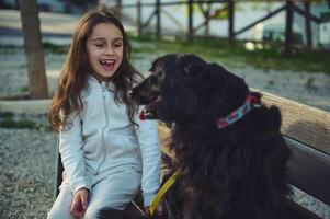 Cute smiling little kid girl playing with her favorite pedigree dog friend while walking outdoors in the city park. Cheerful elementary age child enjoying happy time with her pet in the nature photo