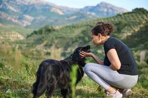 Affectionate young woman embracing her pedigree black cocker spaniel pet dog while walking him in the mountains nature. Playing pets and people concept photo