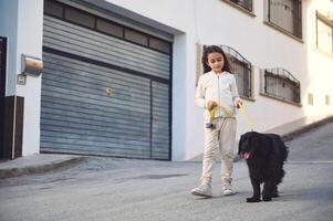 Happy little child girl walking her dog on leash on the city street photo