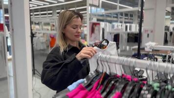 un joven mujer elige un camisa en un ropa Tienda video