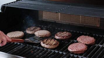 il superiore fuori uso, vicino su Visualizza di parecchi hamburger cucinando su il griglia. qualcuno è capovolgimento il hamburger e il fiamme siamo alto. video