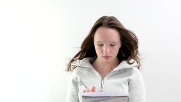 un joven Adolescente niña escribe en un grande blanco computadora portátil, ella piensa acerca de un ensayo, viene arriba con historia, joven autor, adolescencia, picaduras su bolígrafo y mira a lado, Sueños, piensa, planes, escribe planes video