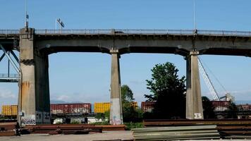 Pattullo Bridge over Fraser River train passing under bridge. close-up shot from technological site scattered iron beams for the construction of new bridge against the backdrop of mountains and sky video