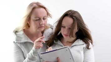 mother and daughter solve math problems together doing homework Girl writes in notebook with pen woman shows finger hint mutual understanding help good relationships adolescence in white studio video