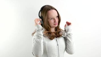 tiener- meisje luistert naar muziek- in groot professioneel hoofdtelefoons Aan een wit achtergrond sport- pak voorzichtig glimlacht mooi tiener adolescentie video