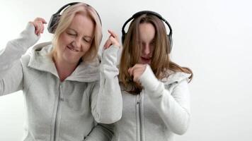 mulher e menina mãe e filha ouvindo para música em fones de ouvido dançando dentro a mesmo roupas dois gerações mútuo compreensão amigos em uma branco fundo dançando menina cantando video
