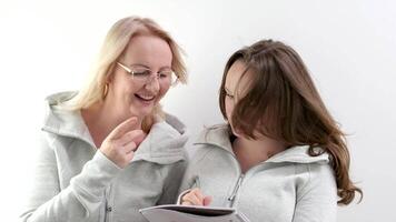 maman et fille Faire devoirs, femme portant lunettes, fille en essayant à écrire, elles ou ils sont en riant, souriant, dépenses agréable temps, expliquant à enfant, surprendre, montrer du doigt avec main à bloc-notes, carnet video