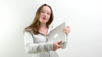 giovane adolescenziale ragazza gioisce a il nuovo il computer portatile abbracci sorridente grigio aggeggio si chiude guardare a esso tenerezza gioia regalo vincente su un' bianca sfondo giovane donna studio video
