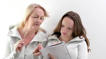 mamá y hija haciendo tarea, mujer vistiendo anteojos, niña molesto a escribir, ellos son reír, sonriente, gasto agradable tiempo, explicando a niño, sorpresa, señalando con mano a bloc, cuaderno video