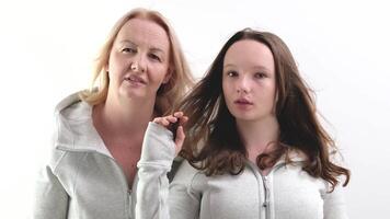 avvicinamento facce di europeo donne, un adulto e un' giovane ragazza guardare in il telaio, madre e figlia puntamento con un' dito, rottura capelli bianca sfondo video